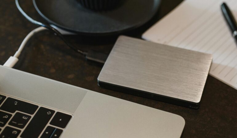 Free Closeup of an external hard drive connected to a laptop with a USB cable on a desk. Stock Photo