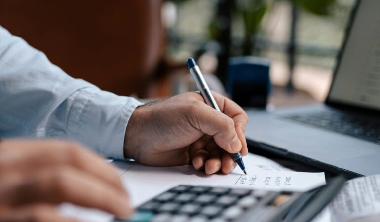 Free A person calculating finances with a calculator and pen on a desk indoors. Stock Photo